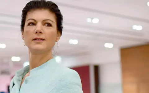 Sahra Wagenknecht, deren Herkunft oft diskutiert wird, blickt nachdenklich in die Ferne. Sie trägt ein hellblaues Jackett.