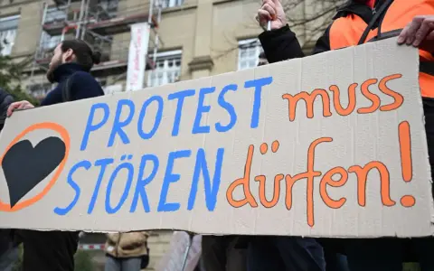 Menschen halten ein Schild mit der Aufschrift "PROTEST muss STÖREN dürfen!". Ein schwarzes Herz in einem orangen Kreis symbolisiert ziviler ungehorsam Beispiele.