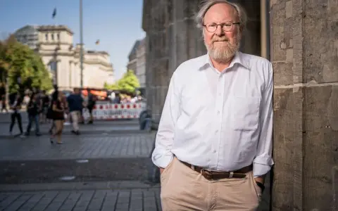 Wolfgang Thierse, lächelnd, lehnt an einer Säule vor dem Reichstagsgebäude in Berlin.