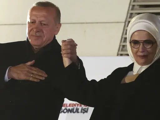 Erdogan und seine Frau, die ein Kopftuch trägt, halten Händchen.