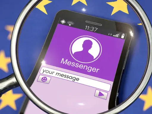 Lupe über Smartphone mit Messenger-App vor EU-Flagge. Diskussionen über Chatkontrolle EU.