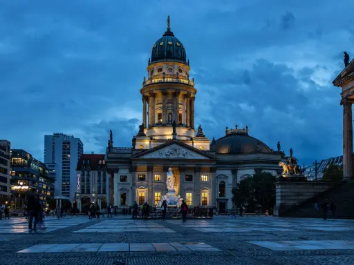 Der Gendarmenmarkt in Berlin bei Dämmerung. Die Kuppeln des Deutschen und Französischen Doms, Zeugen der Hugenotten in Berlin, erstrahlen im Licht.
