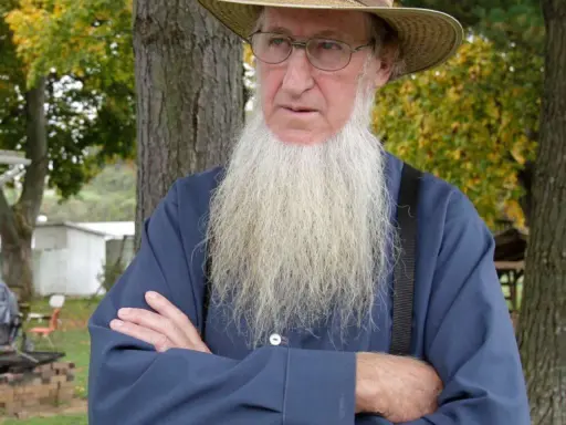 Ein älterer Amish-Mann mit langem, weißem Bart und Strohhut blickt nachdenklich.