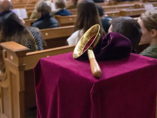 Gabe beim Gottesdienst: Eine Glocke auf einem mit Samt bezogenen Tisch, während Gläubige in den Kirchenbänken sitzen.