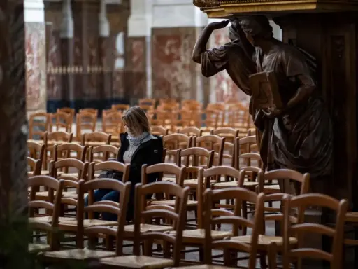 Frau sitzt allein in einer leeren Kirche, umgeben von Stuhlreihen. Eine Statue wacht über sie. Ein Moment der Stille, vielleicht ein Gebet oder eine Reflexion, bevor die "la cimade" beginnt.