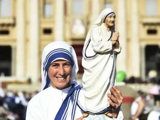Eine Frau im Habit von Mutter Teresa hält eine Statue von ihr. Sie zeigt, was Mutter Teresa gemacht hat: Nächstenliebe und Hilfe für Bedürftige.