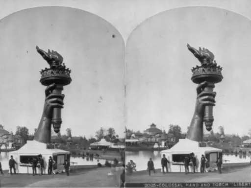 Die Hand mit der Fackel der Freiheitsstatue, ein Werk der freiheitsstatue erbauer, ragt über einem Pavillon auf. Im Hintergrund ist eine Parklandschaft mit einem See und Gebäuden zu sehen.