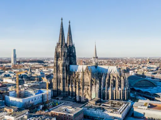Majestätische gotische Kirchen ragen über einer Stadt auf. Der Kölner Dom, ein Meisterwerk gotischer Architektur, dominiert die Skyline.