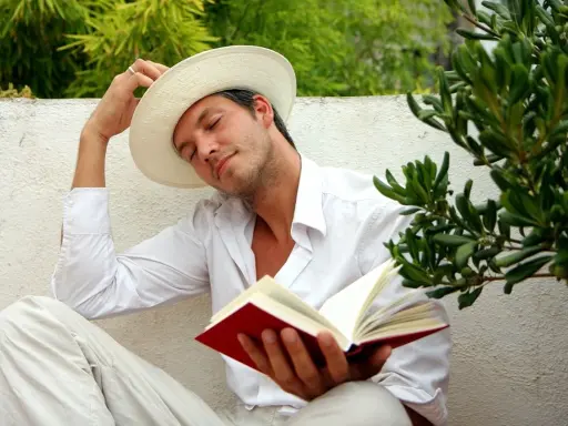 Ein Mann in weißem Hemd und Hut liest ein Buch, genießt die Ruhe. Er verkörpert, was sind Hedonisten: Menschen, die das Leben und seine Freuden suchen.