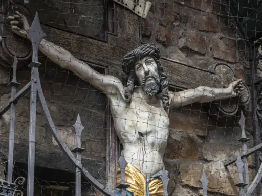 Skulptur Jesu am Kreuz, die an die Frage erinnert, warum wurde Jesus gekreuzigt. Die Darstellung ist durch ein Gitter geschützt.
