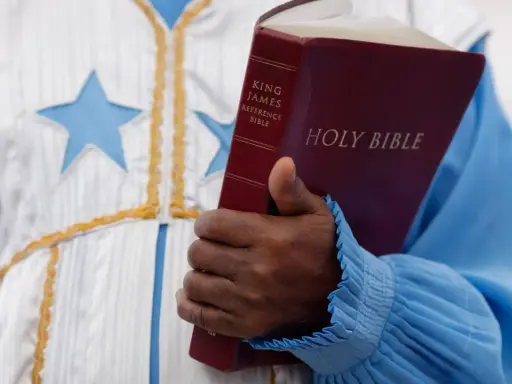Eine Hand hält eine King James Bibel. Der **neues testament inhalt** wird hier durch das Buch repräsentiert, das in einer festlichen Robe mit Sternen getragen wird.