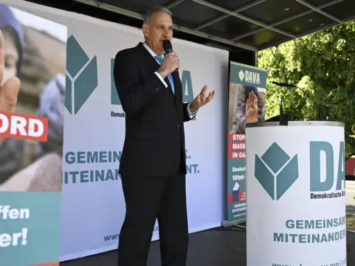 Mann spricht ins Mikrofon vor DAVA-Banner. "Gemeinsam Miteinander" steht auf den Bannern.