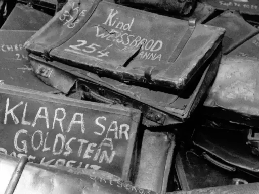 Stapel von alten Koffern, beschriftet mit Namen wie "Klara Goldstein" und "Kind Weissbrod Johanna". Diese Auschwitz Koffer sind ein trauriges Zeugnis der Vergangenheit.