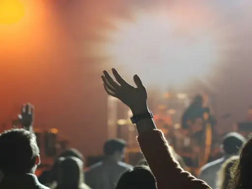 Eine Hand hebt sich im Scheinwerferlicht, während eine Menge bei einem Konzert jubelt. Dies spiegelt die lebendige Pfingstler Erziehung wider, die Gemeinschaft und Ausdruck fördert.