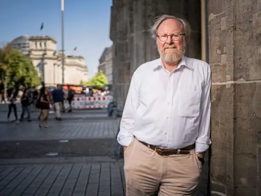 Wolfgang Thierse, lächelnd, lehnt an einer Säule vor dem Reichstagsgebäude in Berlin.