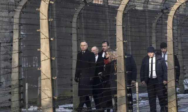 Eine Gruppe von Menschen, darunter ein Mann in einem langen schwarzen Mantel, geht hinter Stacheldraht entlang. Die Szene erinnert an die Verfolgung von Dietrich Bonhoeffer.