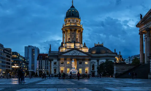 Der Gendarmenmarkt in Berlin bei Dämmerung. Die Kuppeln des Deutschen und Französischen Doms, Zeugen der Hugenotten in Berlin, erstrahlen im Licht.