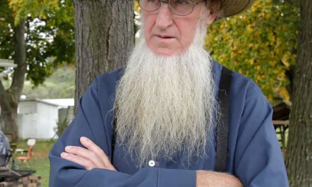 Ein älterer Amish-Mann mit langem, weißem Bart und Strohhut blickt nachdenklich.
