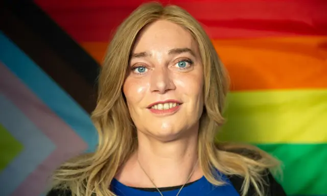 Markus Ganserer lächelt vor einer Pride-Flagge.