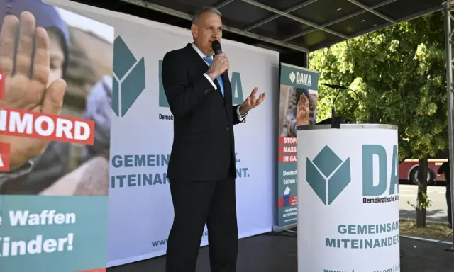 Mann spricht ins Mikrofon vor DAVA-Banner. "Gemeinsam Miteinander" steht auf den Bannern.