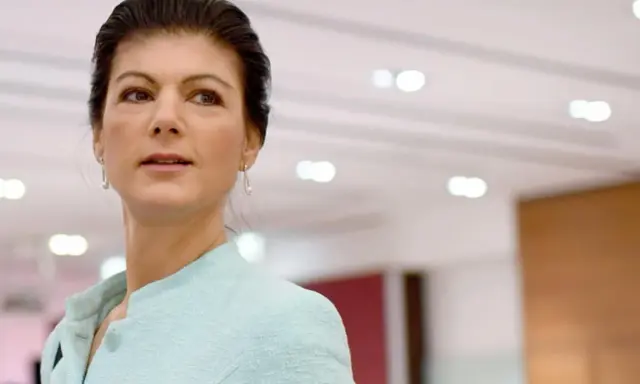 Sahra Wagenknecht, deren Herkunft oft diskutiert wird, blickt nachdenklich in die Ferne. Sie trägt ein hellblaues Jackett.