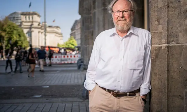 Wolfgang Thierse, lächelnd, lehnt an einer Säule vor dem Reichstagsgebäude in Berlin.