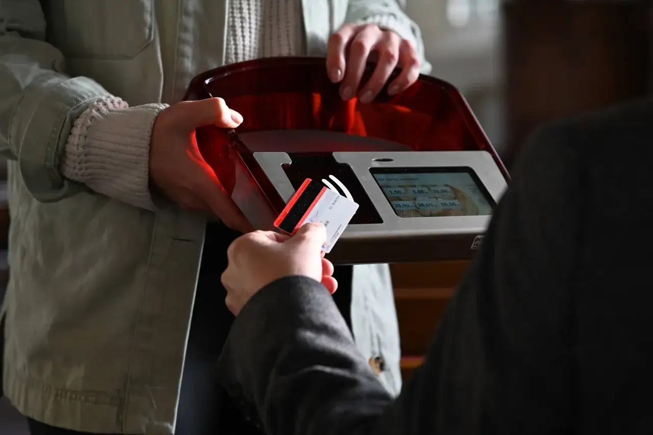 Gabe beim Gottesdienst: Eine Person hält eine Karte an ein Lesegerät, um einen Betrag zu spenden.