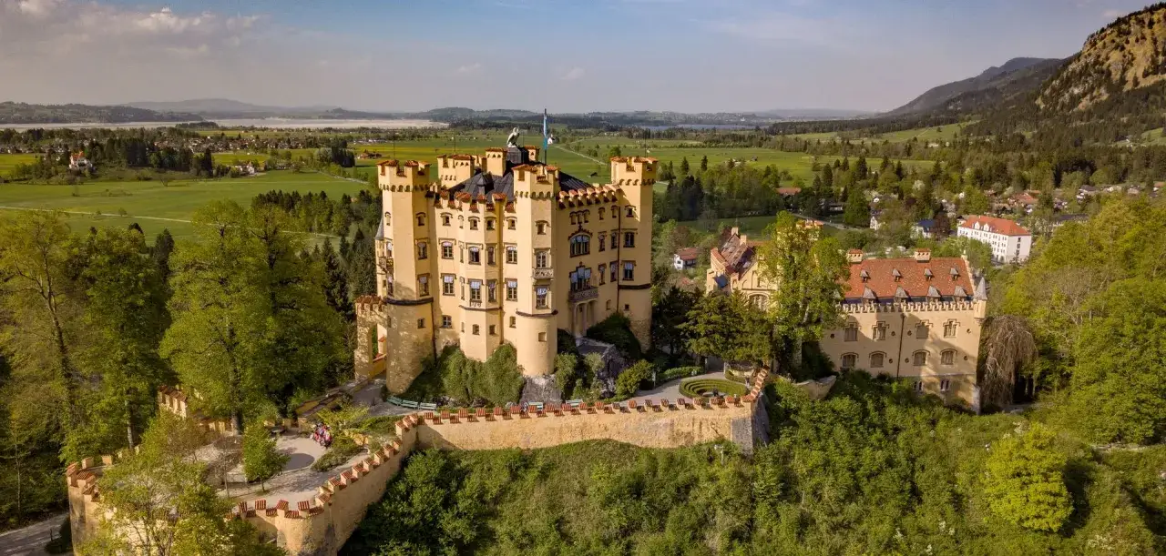 Gelbes Schloss auf einem H&uuml;gel, umgeben von gr&uuml;nen W&auml;ldern und Feldern. Ein Teil des Wittelsbacher Ausgleichsfonds, der Geschichte und Natur vereint.