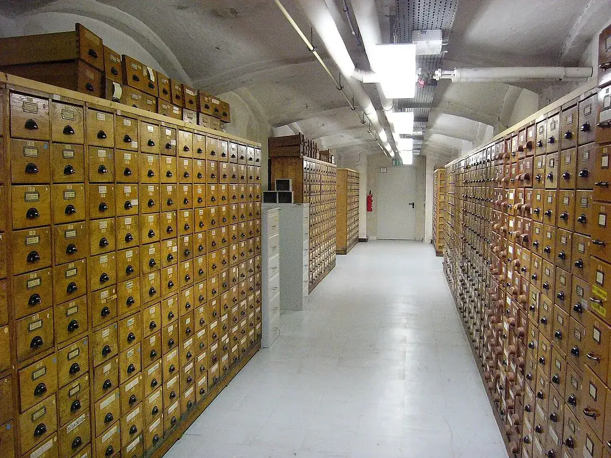 Ein langer Gang mit Reihen von Holzschubladen, die an eine Bibliothek erinnern. Hier wird die Bedeutung von