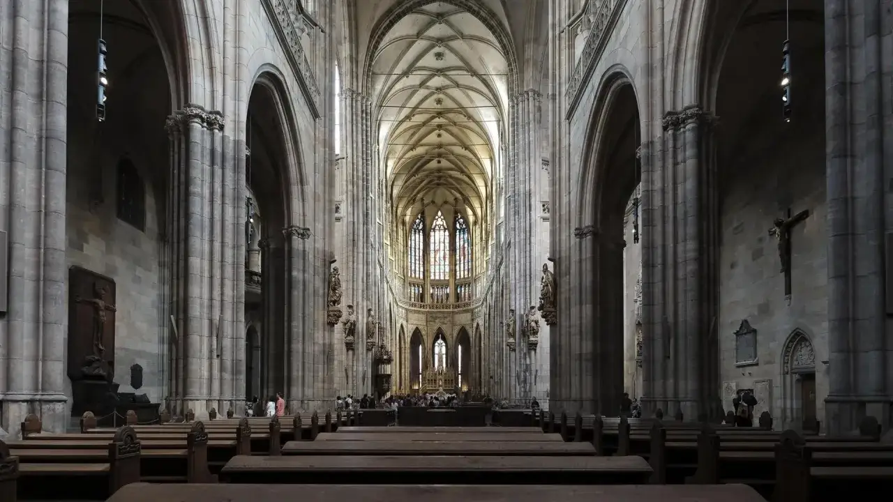 Das Innere einer beeindruckenden gotischen Kirche mit hohen Gewölben, Buntglasfenstern und Holzbänken.