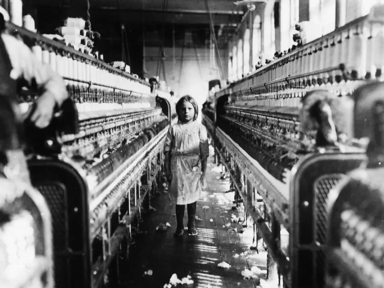 Ein junges Mädchen steht in einer Fabrik zwischen Spinnmaschinen. Ein trauriges Zeugnis von Kinderarbeit in Deutschland.
