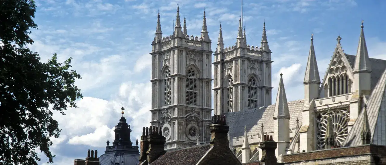 Zwei Türme der Westminster Abbey, einer berühmten anglikanischen Kirche, ragen unter einem blauen Himmel mit Wolken empor.