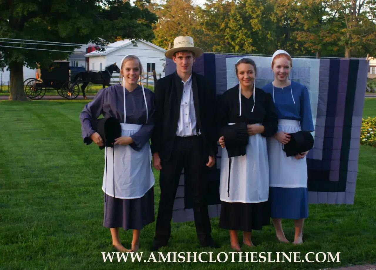 Ein Amish-Mann mit Hut steht neben drei jungen Frauen in traditioneller Kleidung. Im Hintergrund eine Pferdekutsche.