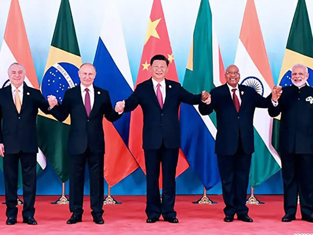 Fünf Staatschefs der BRICS-Staaten halten Händchen vor ihren Flaggen. Ihre gemeinsamen Ziele werden hier symbolisiert.