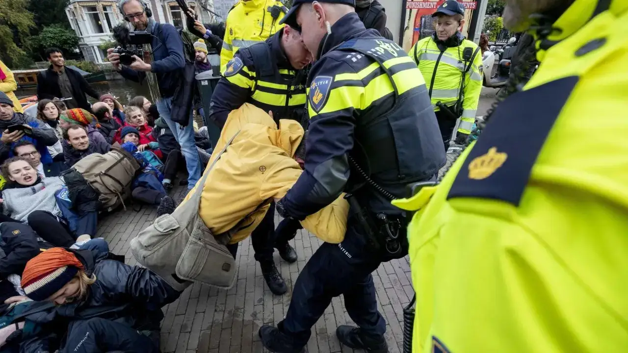 Polizisten tragen Demonstranten weg, die friedlich sitzen. Ein Kameramann filmt die Szene. Solche Szenen sind Beispiele für zivilen Ungehorsam.