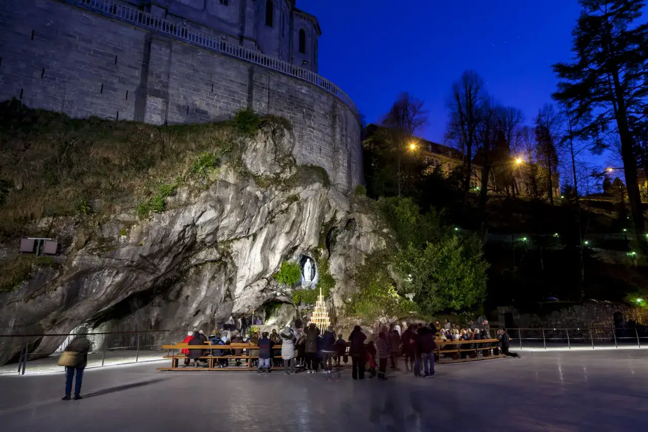 Pilger versammeln sich vor der Grotte in Lourdes, wo die Jungfrau Maria erschien. Ein Kerzenlicht-Altar und eine Marienstatue erinnern an das Wunder von Lourdes, wahre Geschichte.