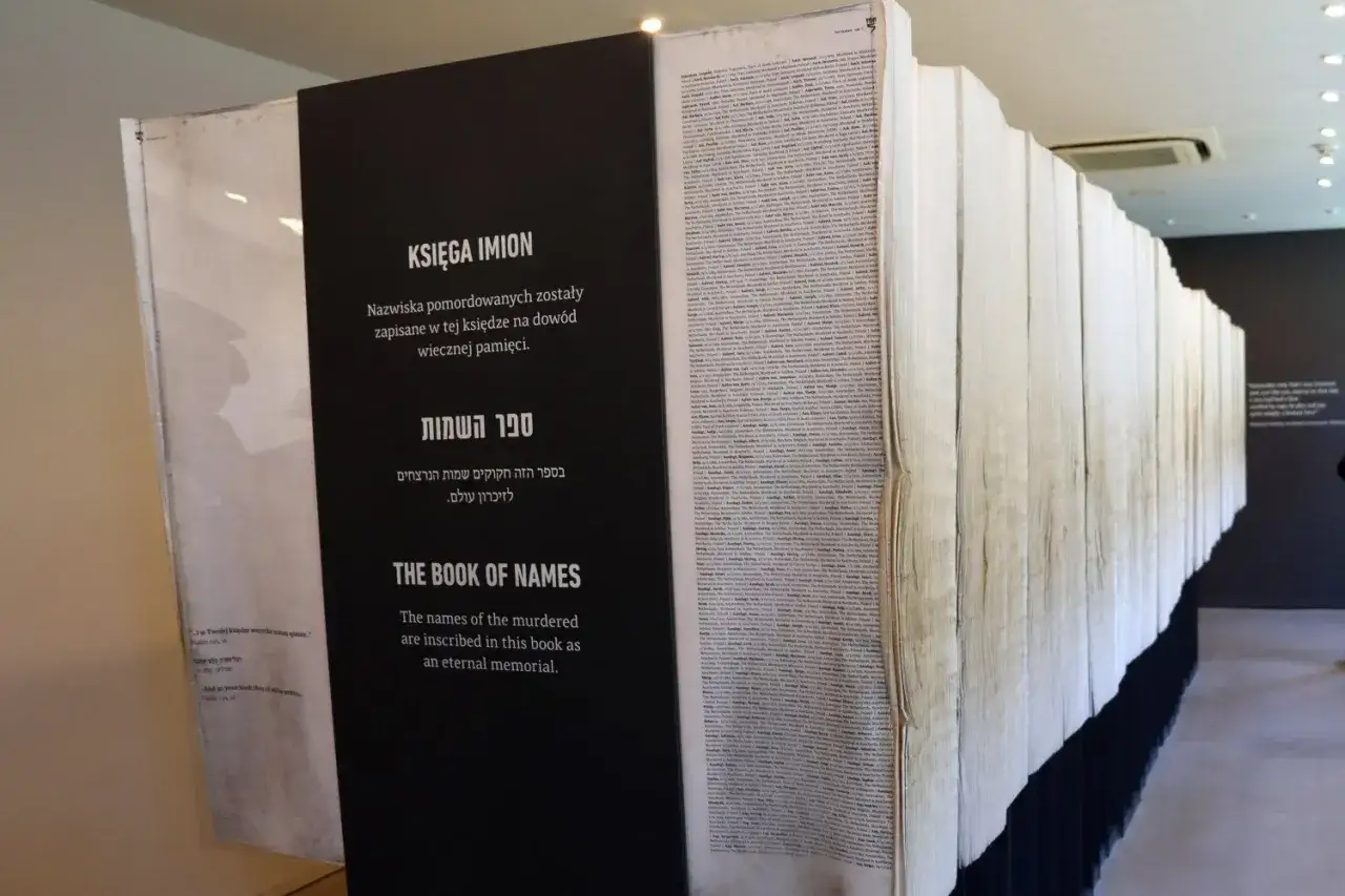 Ein riesiges Buch mit Namen von Opfern des Holocaust, das an die Gräueltaten in Auschwitz erinnert. Die Seiten sind gefüllt mit den Namen der Ermordeten, ein ewiges Mahnmal.