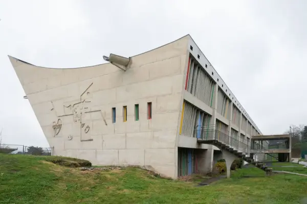 Betonbau mit bunten Fenstern und einer markanten, geschwungenen Form. Ein Meisterwerk des Architekten Le Corbusier.