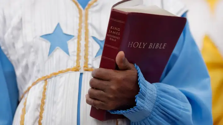 Eine Hand hält eine King James Bibel. Der **neues testament inhalt** wird hier durch das Buch repräsentiert, das in einer festlichen Robe mit Sternen getragen wird.