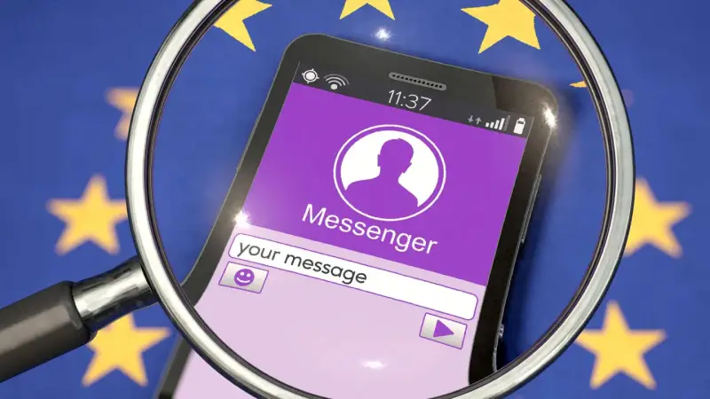 Lupe über Smartphone mit Messenger-App vor EU-Flagge. Diskussionen über Chatkontrolle EU.